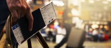 Person holding boarding pass and luggage at airport.